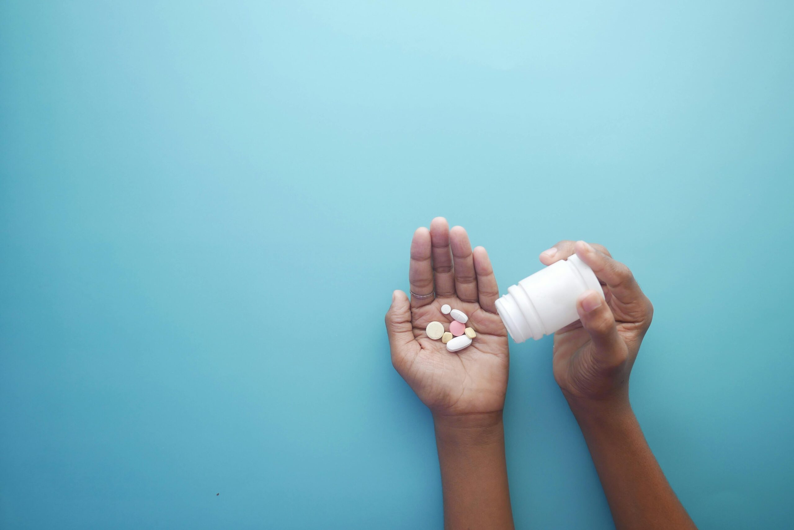 Hands pouring pills from a bottle against a blue background—illustrating the reality of substance misuse that North Star Treatment is committed to addressing with care and support.