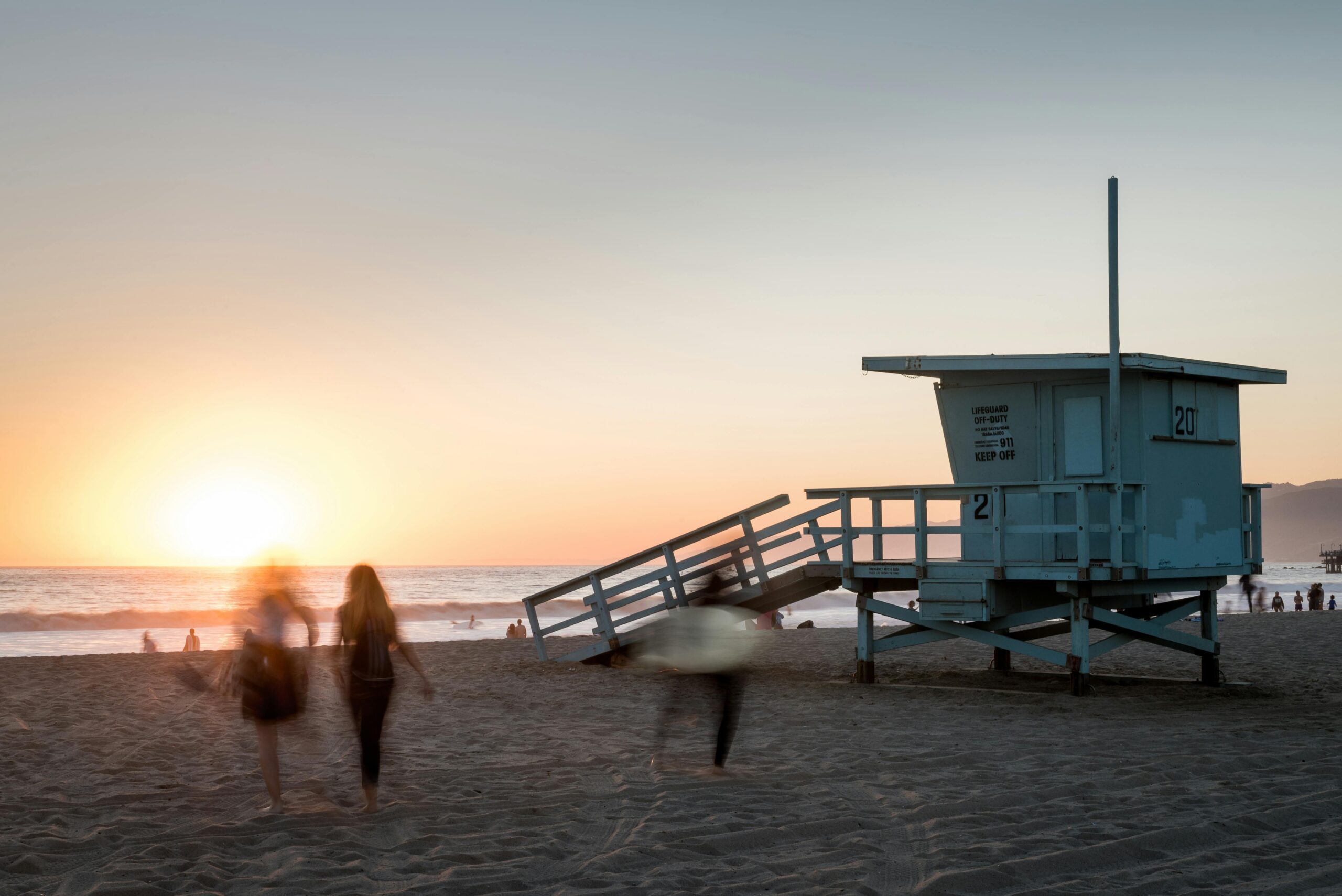 Sunset at a beach with a lifeguard tower and people walking along the shore, symbolizing a fresh start through medical detox at North Star Treatment.